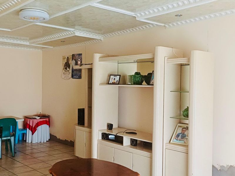 Living room featuring tiled flooring, a decorative coffered ceiling, and built-in display cabinetry, showing signs of wear on the lower wall surfaces.