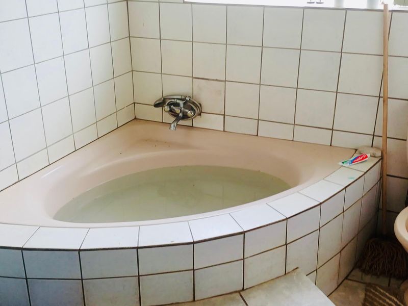 A dated bathroom featuring a built-in corner bathtub and standard toilet, requiring cosmetic updates to modernize the space.