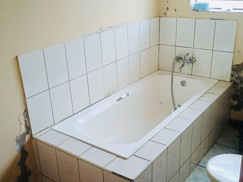 A bathroom featuring a built-in bathtub with chrome fixtures, currently requiring significant wall repairs and cosmetic updates to address visible plaster and paint damage.