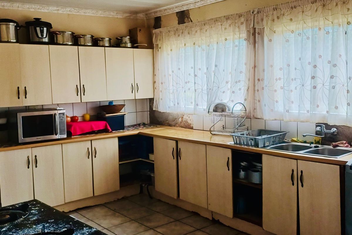 A dated kitchen featuring laminate cabinetry, a double basin sink, and tiled splashbacks, currently showing significant wear to the wall finishes.