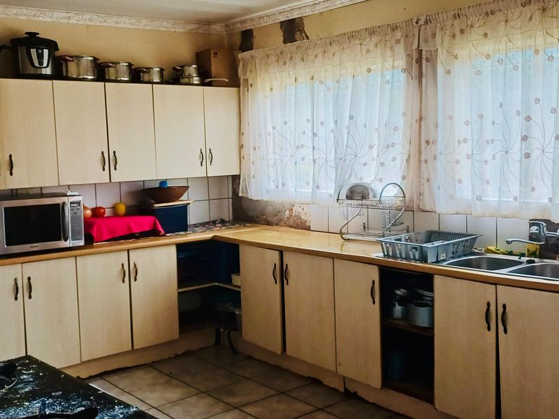 A dated kitchen featuring laminate cabinetry, a double basin sink, and tiled splashbacks, currently showing significant wear to the wall finishes.