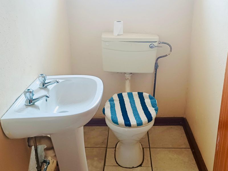 A compact bathroom featuring a pedestal washbasin and a standard toilet with tiled flooring.