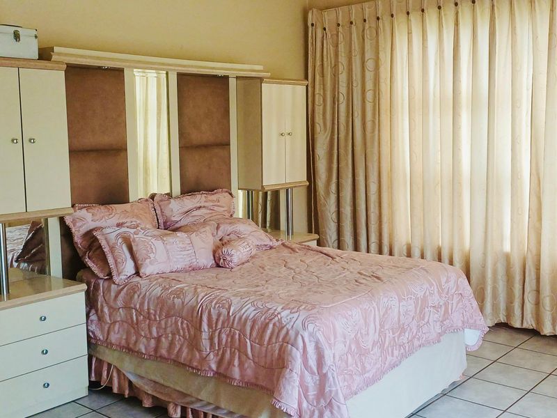 A bedroom featuring tiled flooring and a built-in headboard unit with integrated storage, complemented by floor-to-ceiling curtains.