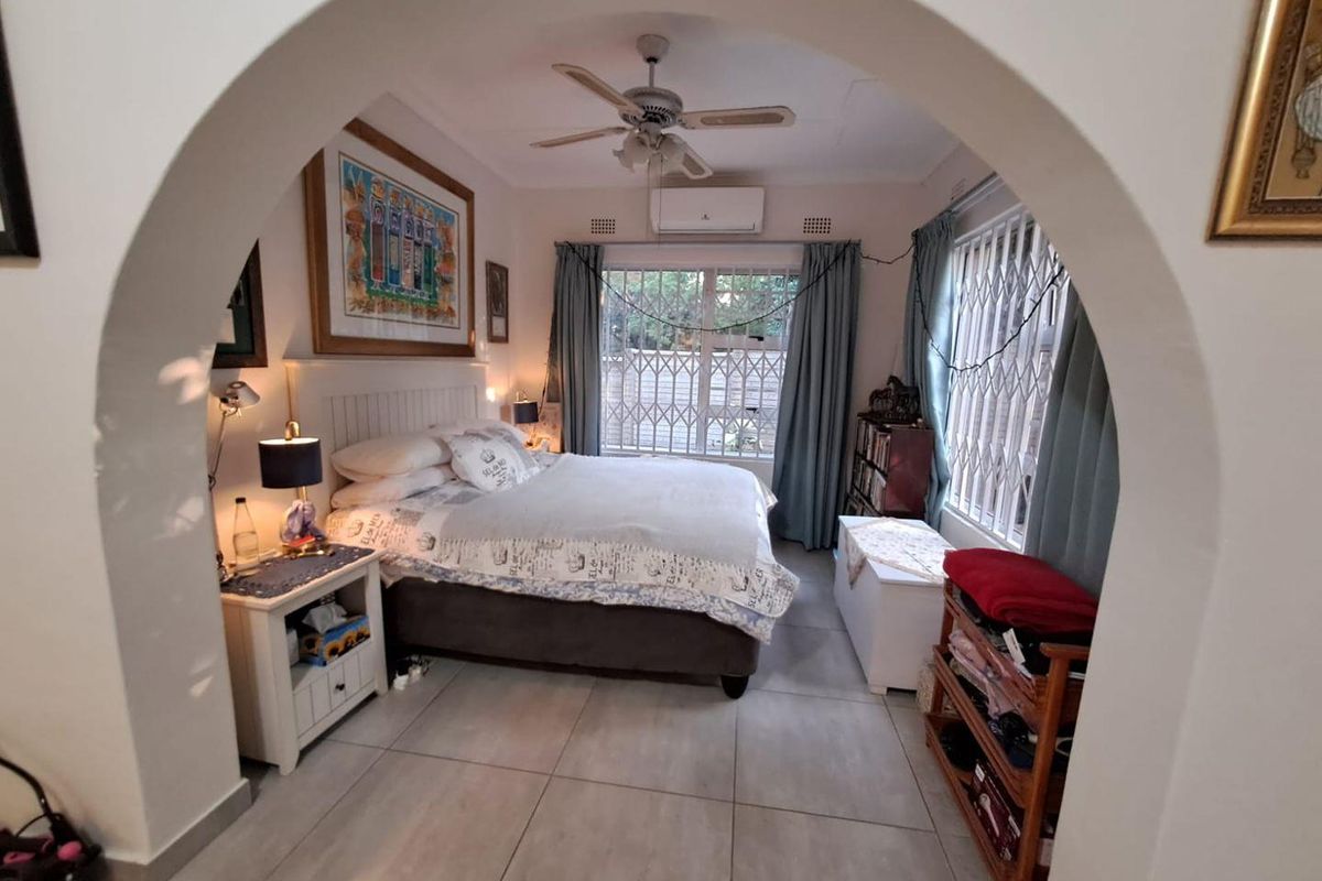 A bedroom featuring tiled flooring, a ceiling fan, and a wall-mounted air conditioning unit, viewed through a decorative arched entryway.