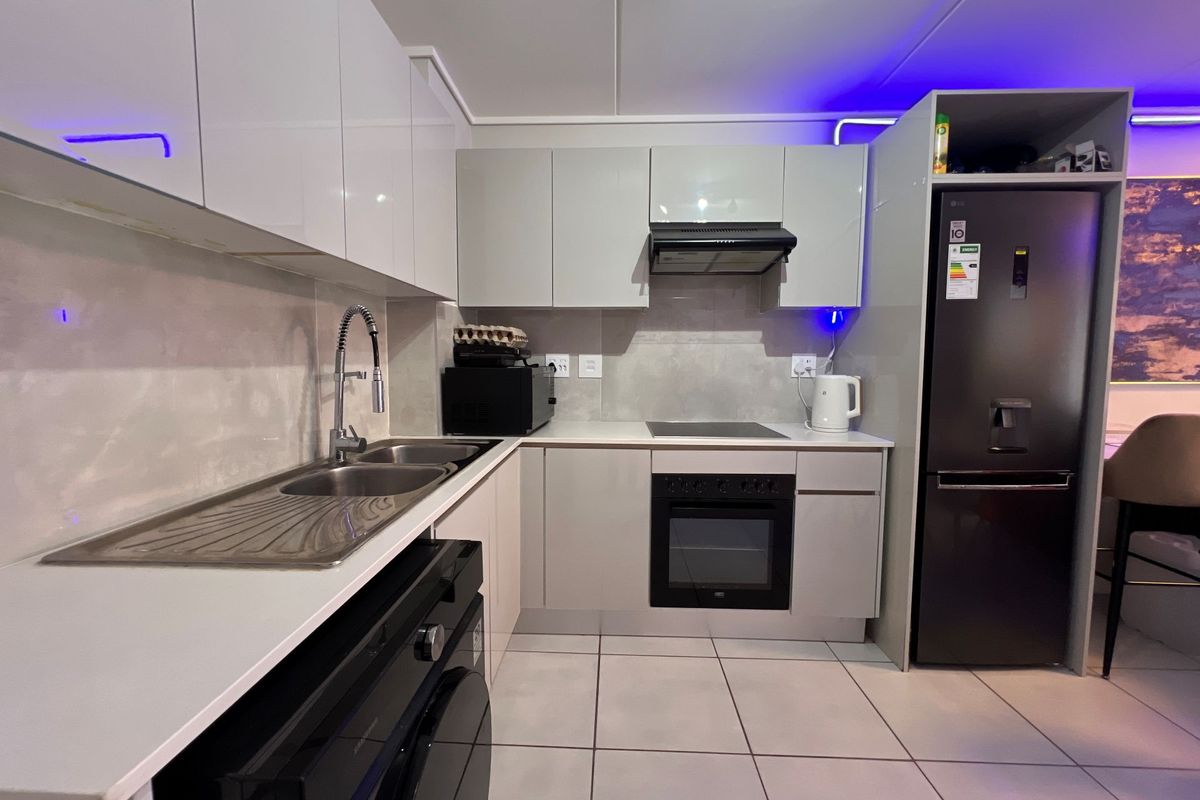 Modern kitchen featuring sleek white cabinetry, stone countertops, integrated appliances including an oven and hob, and contemporary tiled flooring.