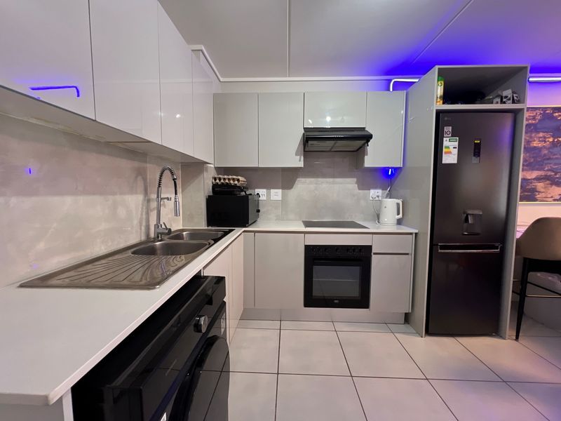 Modern kitchen featuring sleek white cabinetry, stone countertops, integrated appliances including an oven and hob, and contemporary tiled flooring.