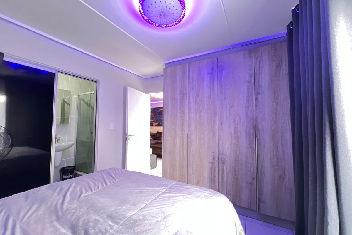 A modern bedroom featuring built-in wood-finish cupboards, tiled flooring, and an en-suite bathroom with contemporary lighting.