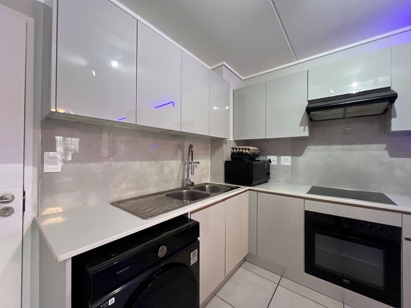 Modern kitchen featuring sleek glossy cabinetry, integrated stainless steel sink, built-in oven, electric hob, and extractor fan with contemporary tiled finishes.