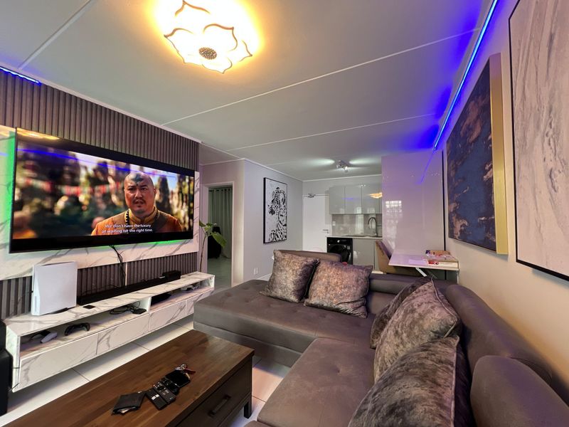Modern open-plan living area featuring a sleek kitchen corner, decorative wall paneling, and integrated ambient lighting, creating a contemporary and functional apartment space.