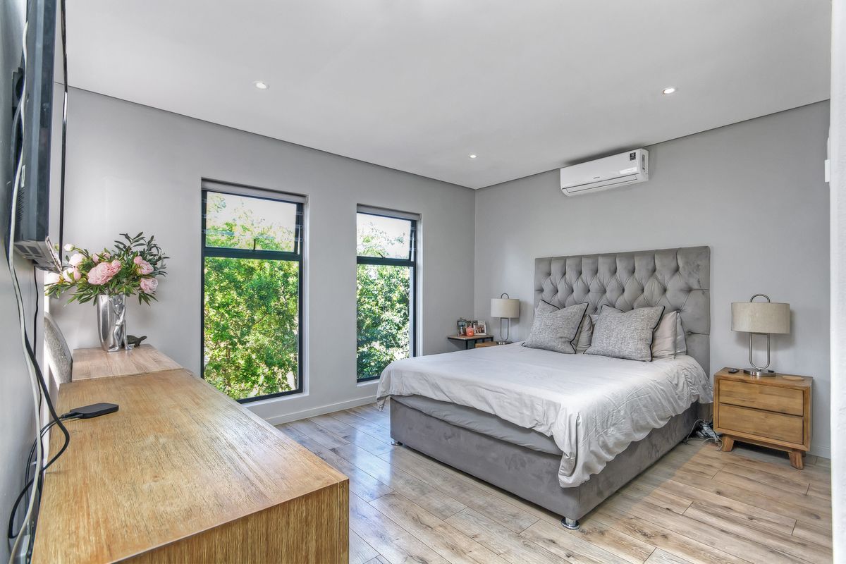 A modern, well-lit bedroom featuring light wood-look flooring, recessed ceiling lighting, and a wall-mounted air conditioning unit.