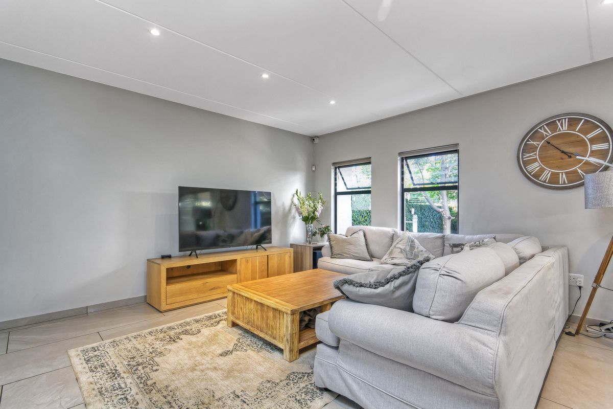 A bright and modern living room featuring tiled flooring, recessed ceiling lighting, and large windows that provide natural light and a view of the garden.