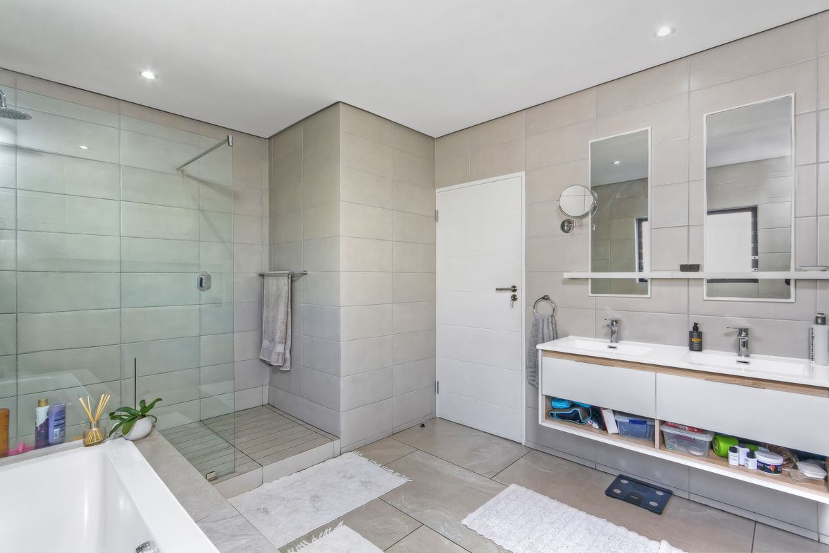 Modern bathroom featuring a double vanity with integrated sinks, a frameless glass walk-in shower, and a separate bathtub with neutral floor-to-ceiling tiling.