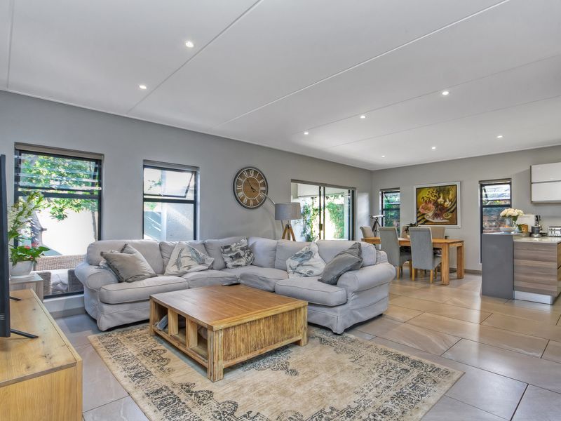 Spacious open-plan living and dining area featuring large format floor tiles, recessed ceiling lighting, and seamless flow to the kitchen and outdoor patio.