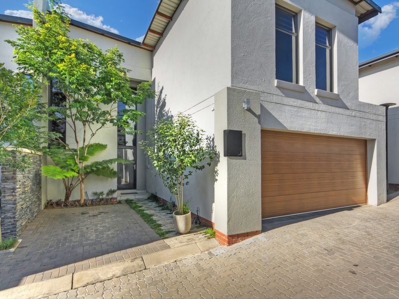 Modern townhouse exterior featuring a paved driveway, integrated single garage with wood-look door, and a landscaped entrance path.