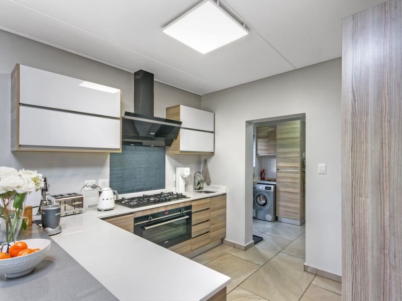 Modern kitchen featuring sleek cabinetry, stone countertops, built-in oven, gas hob, and extractor fan, with an adjacent scullery area.