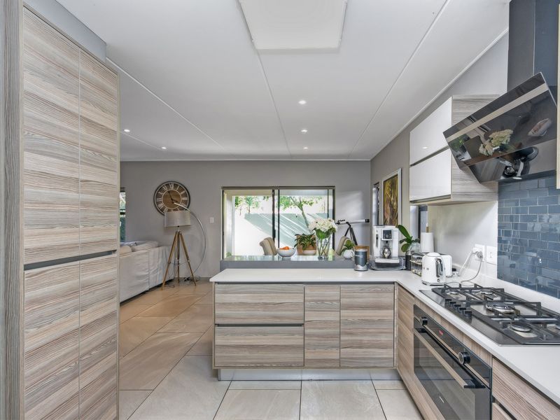 Modern open-plan kitchen featuring wood-grain cabinetry, stone countertops, integrated gas hob, and extractor fan, flowing seamlessly into the adjacent living area.