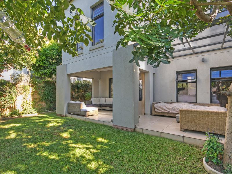 A covered patio area featuring tiled flooring and a structural pergola, seamlessly connecting to a well-maintained private garden.