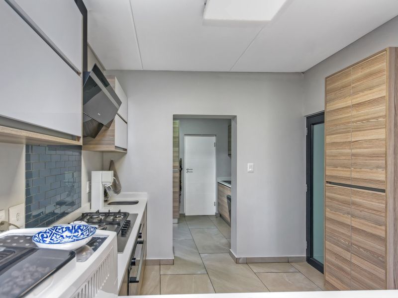 Modern kitchen featuring sleek cabinetry, a built-in gas hob, extractor fan, and tiled flooring, leading into a secondary utility or scullery area.