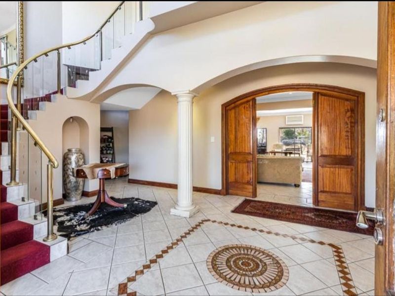 Grand entrance foyer featuring a curved staircase with brass railing, decorative tiled flooring with mosaic inlay, and arched timber double doors leading to living areas.