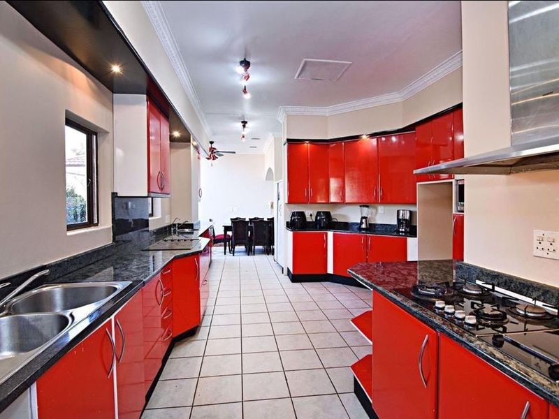 Spacious kitchen featuring vibrant red cabinetry, granite countertops, a built-in gas hob, stainless steel extractor fan, and tiled flooring.