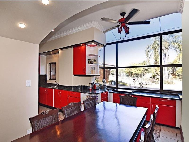 Open-plan kitchen and dining area featuring vibrant red cabinetry, granite countertops, and expansive windows that provide ample natural light and garden views.