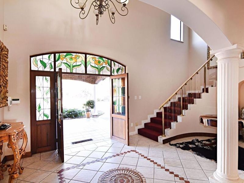 Grand entrance foyer featuring a decorative column, arched stained glass doorway, tiled flooring with inlay detail, and a staircase leading to the upper level.