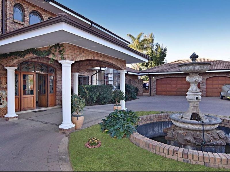 Front entrance view featuring a covered porch with classical columns, a brick facade, a paved driveway, and a decorative stone fountain.