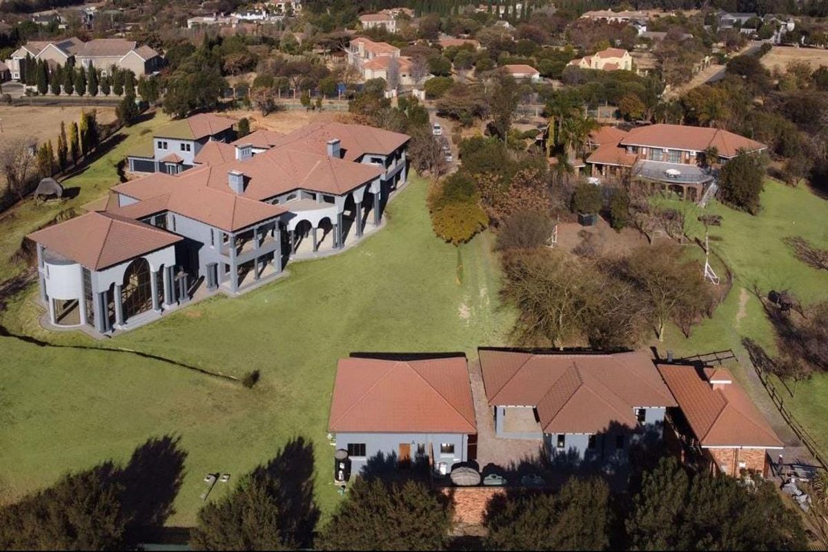 Aerial view of a large residential estate featuring multiple buildings with terracotta tile roofs, expansive lawns, and established landscaping.