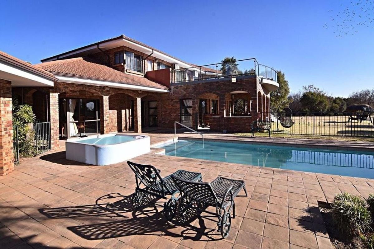 Rear exterior view featuring a swimming pool, built-in jacuzzi, paved patio area, and an upper-level balcony with glass balustrades.