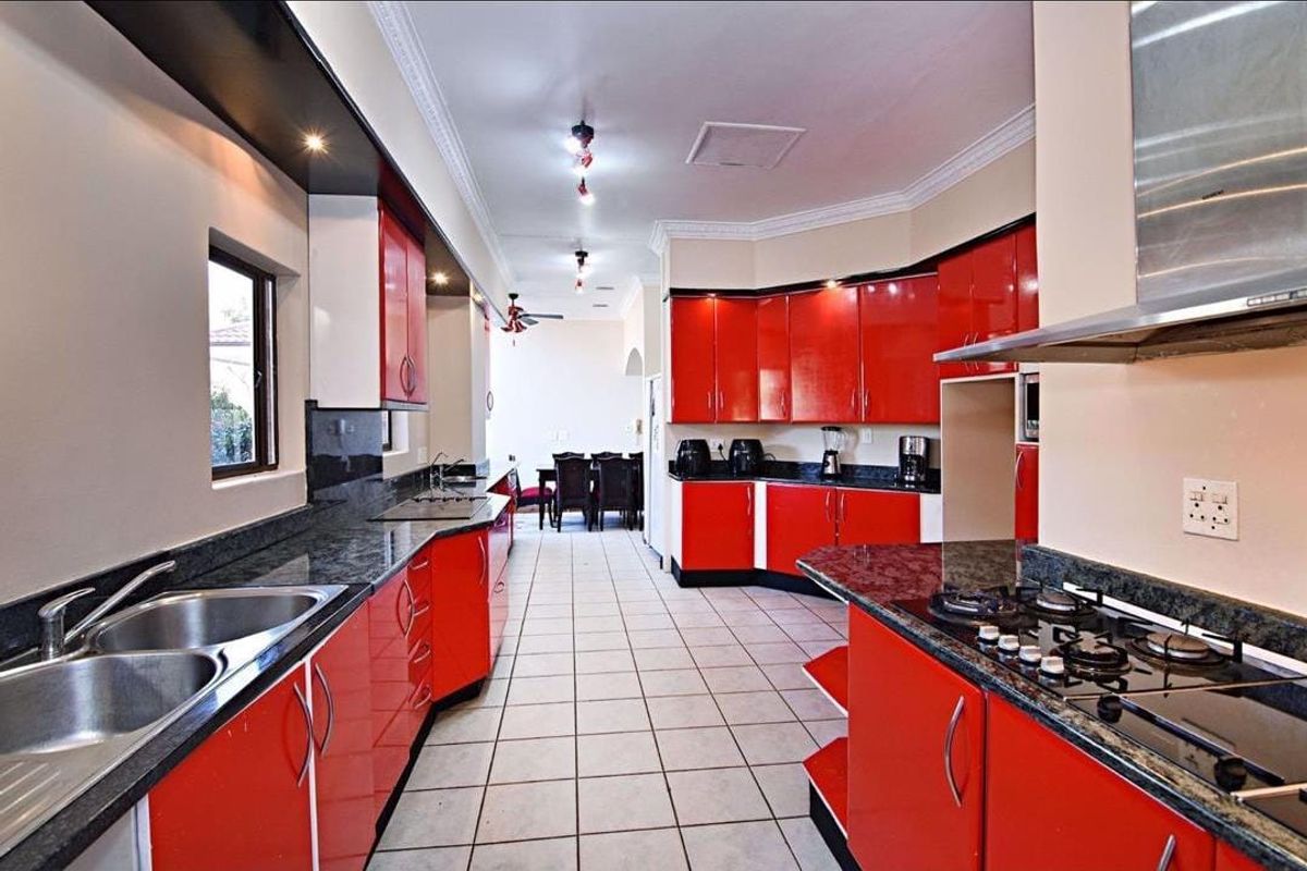 Spacious kitchen featuring vibrant red cabinetry, granite countertops, a built-in gas hob, stainless steel extractor fan, and tiled flooring.
