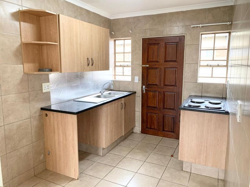 A functional kitchen featuring light wood-finish cabinetry, dark countertops, an integrated electric hob, and full-height wall tiling with direct exterior access.