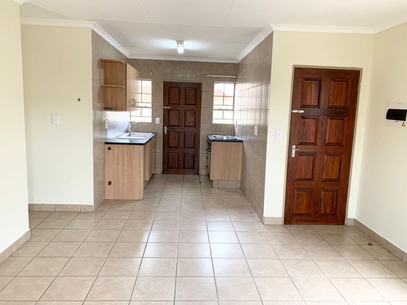 A functional kitchen area featuring tiled flooring, tiled splashbacks, laminate cabinetry, and a freestanding stove, presented in a clean, empty space.