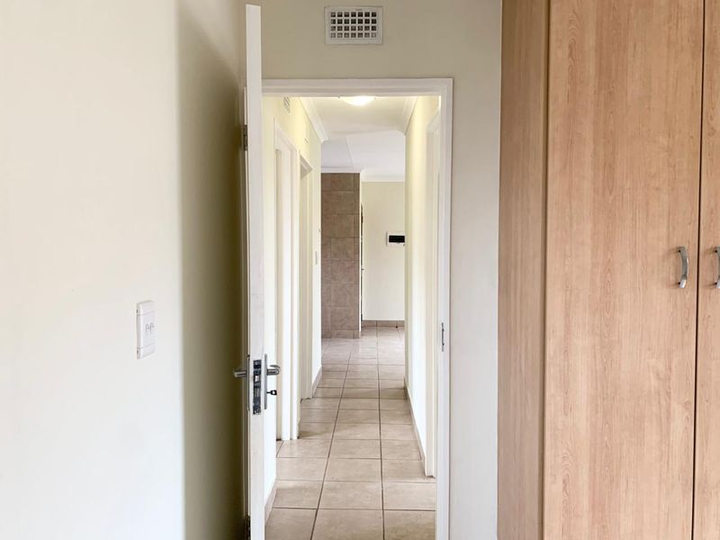 A clean, tiled hallway connecting interior spaces, featuring built-in wooden cupboards and neutral wall finishes.