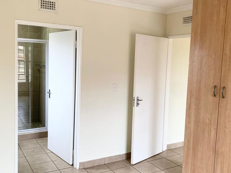 A functional hallway featuring tiled flooring, built-in wooden cupboards, and access to adjacent rooms, including a tiled bathroom area.