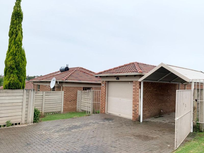 Front exterior view of a townhouse featuring a brick facade, tiled roof, single garage, attached carport, and a paved driveway.