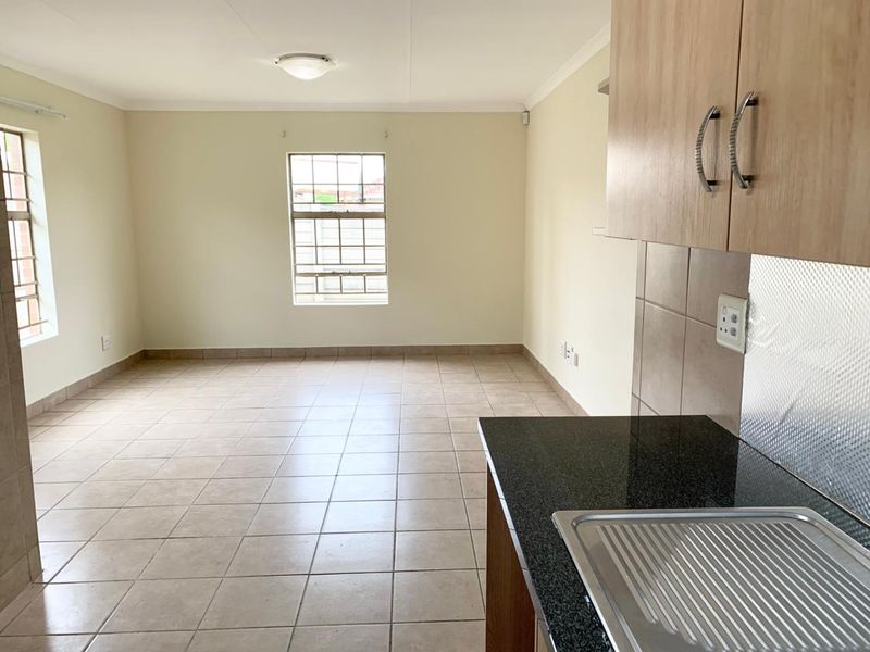An open-plan living and kitchen area featuring neutral tiled flooring, built-in cabinetry with granite countertops, and natural light through security-fitted windows.