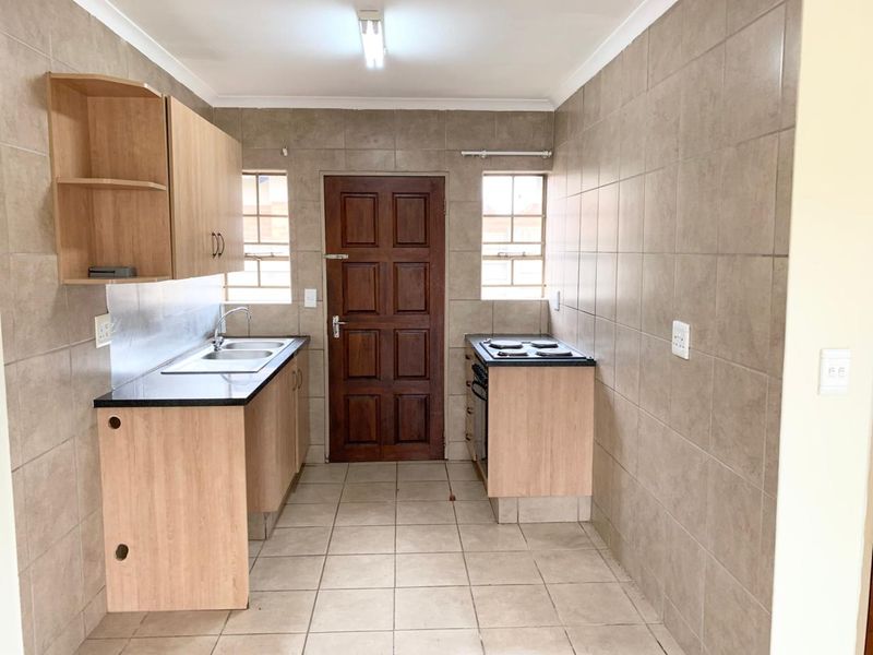 A functional kitchen featuring tiled walls and flooring, built-in cabinetry, a double sink, and a freestanding stove with direct access to the exterior.