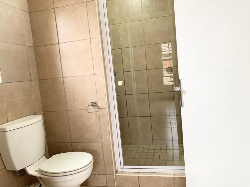 A functional bathroom featuring a shower enclosure and tiled finishes, presenting a clean but dated aesthetic.