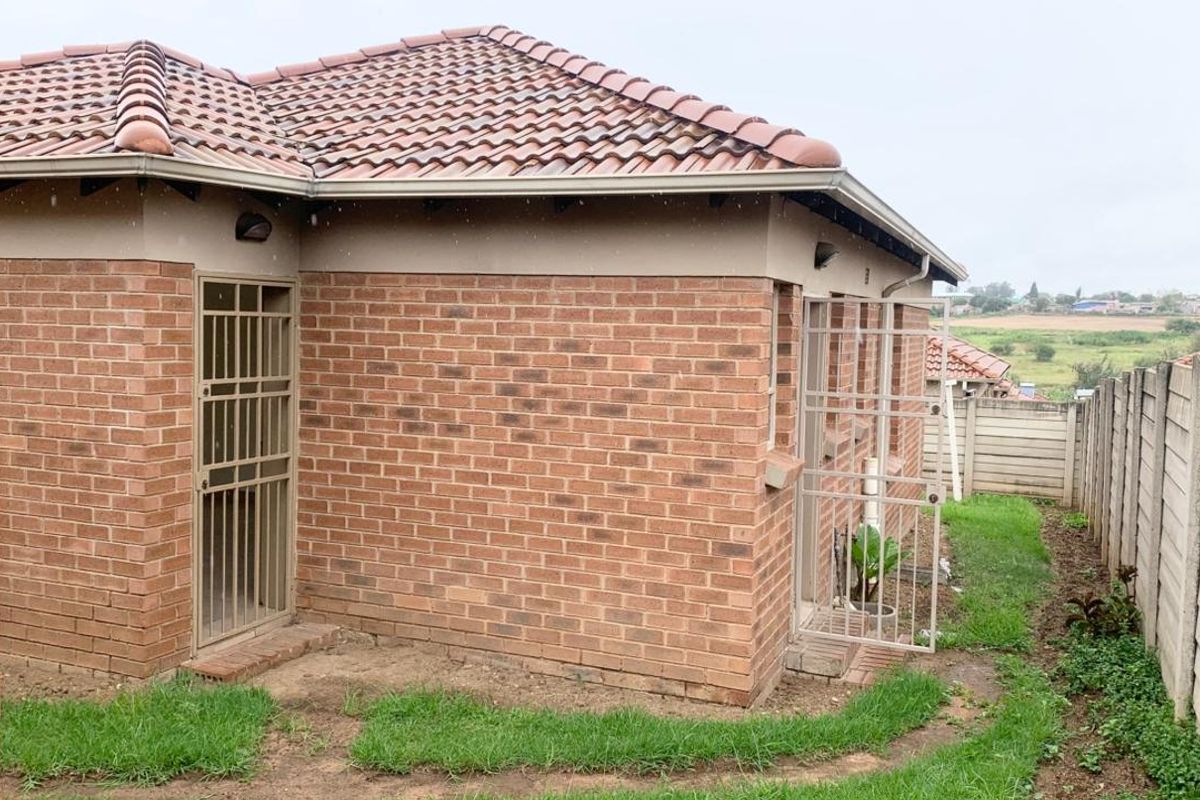 Rear view of a face brick townhouse featuring a tiled roof, security gates, and a precast concrete boundary wall with surrounding garden space.