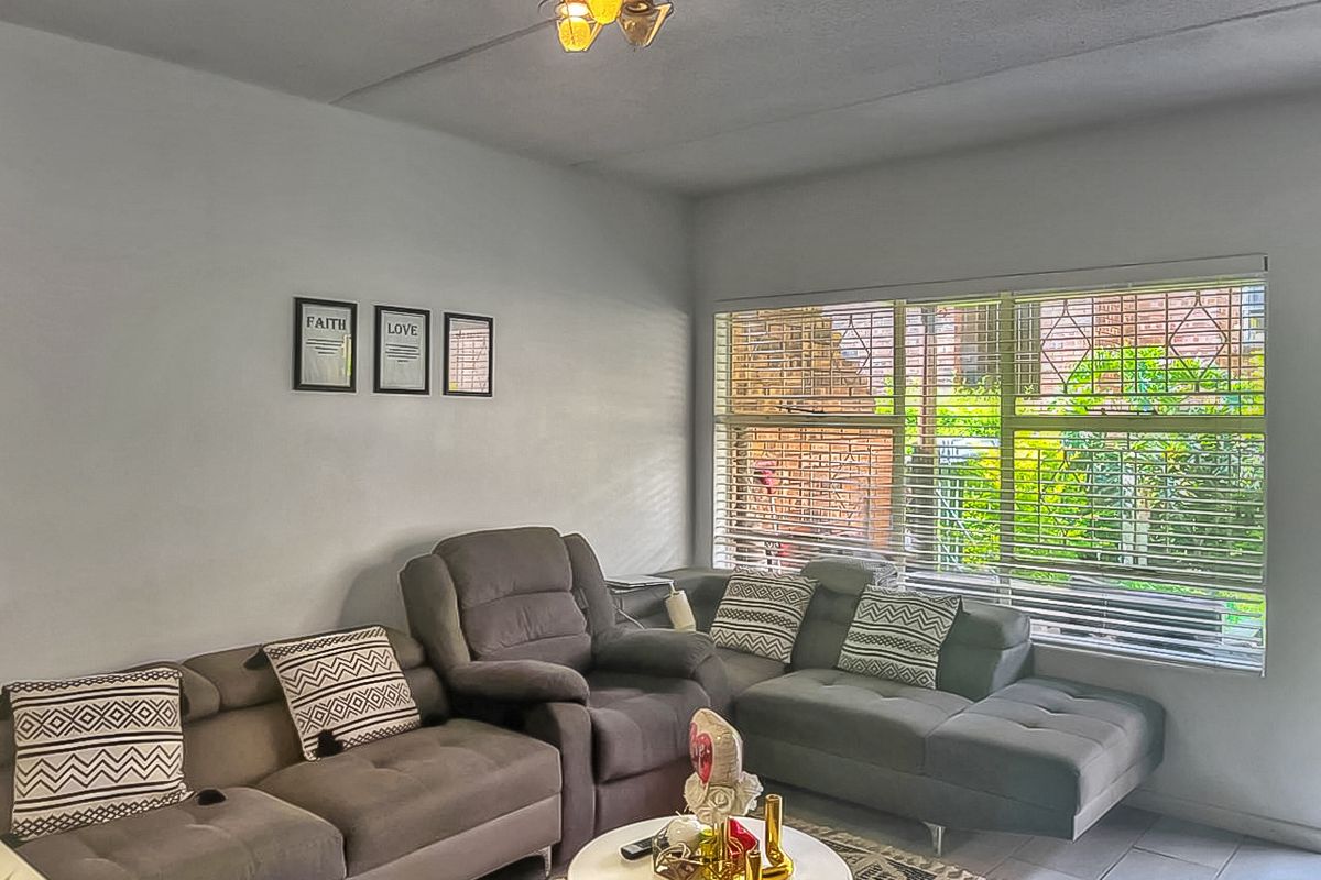A comfortable living room featuring large windows with horizontal blinds, tiled flooring, and a central ceiling light fixture.