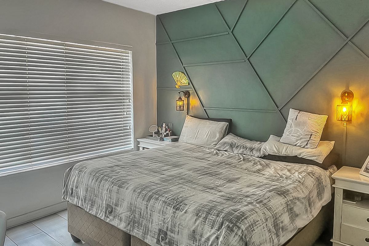 A well-maintained bedroom featuring a decorative geometric accent wall, tiled flooring, and fitted window blinds.