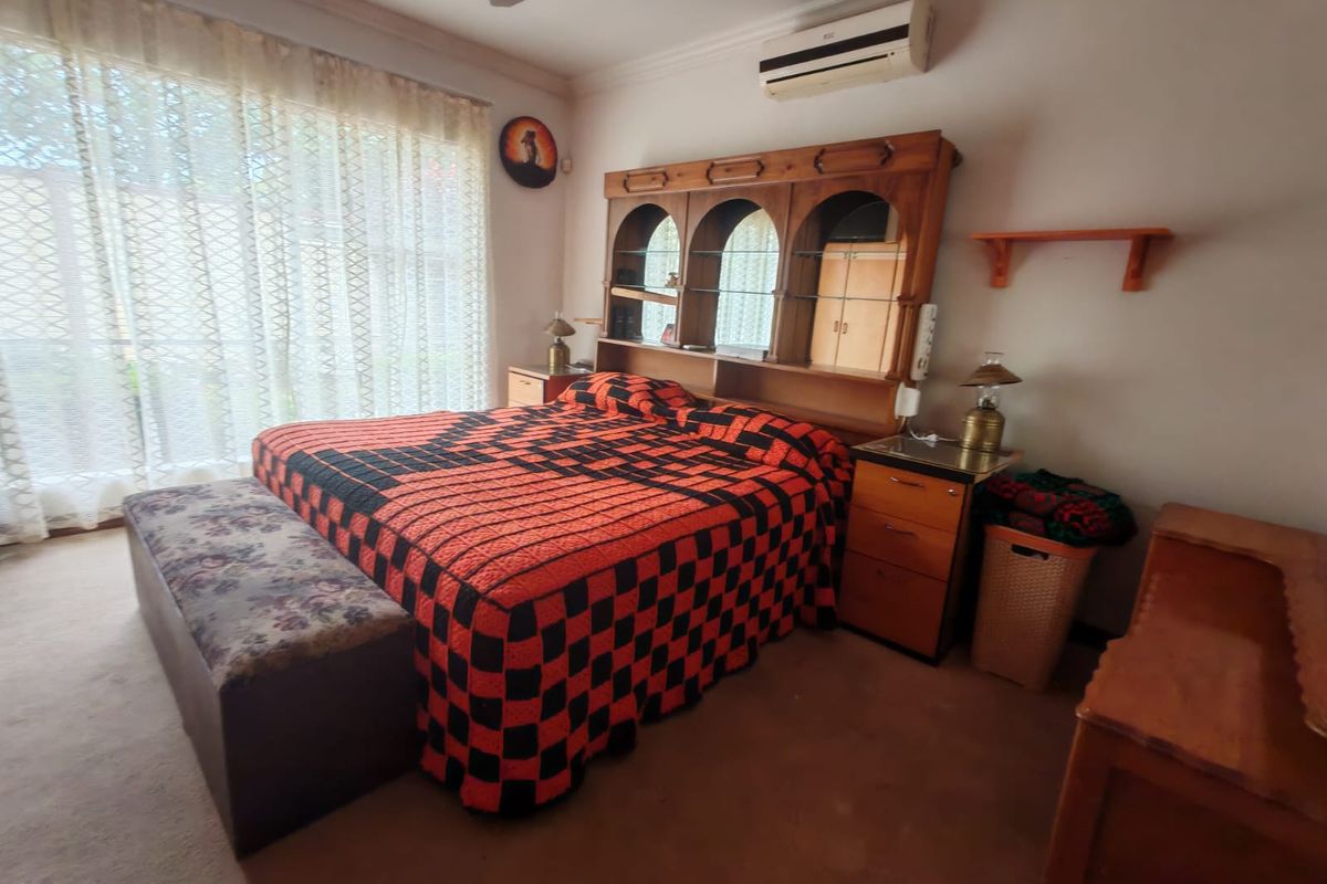 A bedroom featuring a wall-mounted air conditioning unit, large sliding glass doors with curtains, and carpeted flooring.