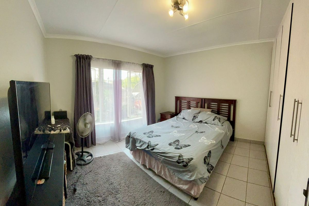 A functional bedroom featuring tiled flooring, built-in cupboards, and natural light through a window with curtains.