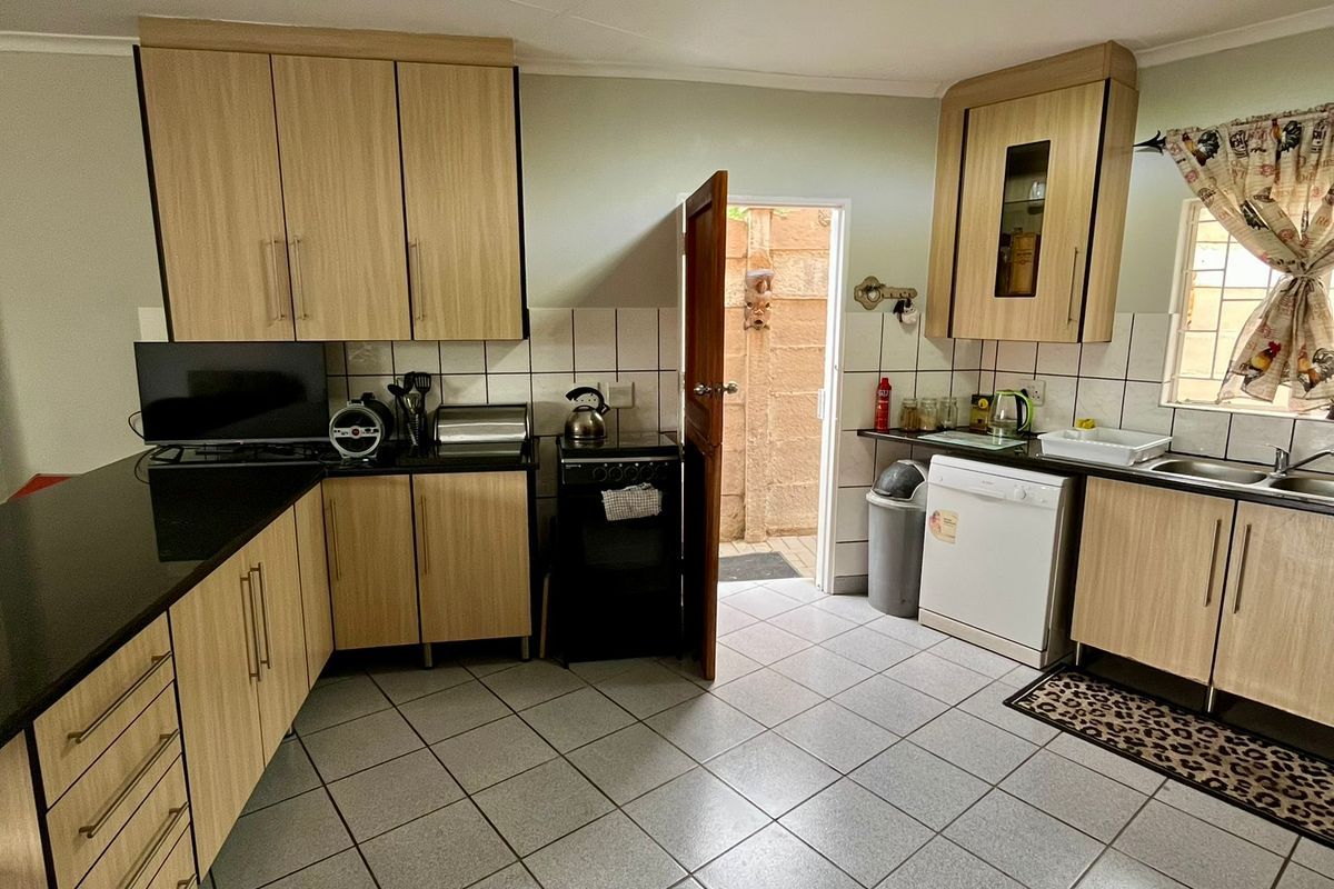 A functional kitchen featuring light wood-tone cabinetry, black granite countertops, tiled flooring, and direct access to an exterior courtyard area.