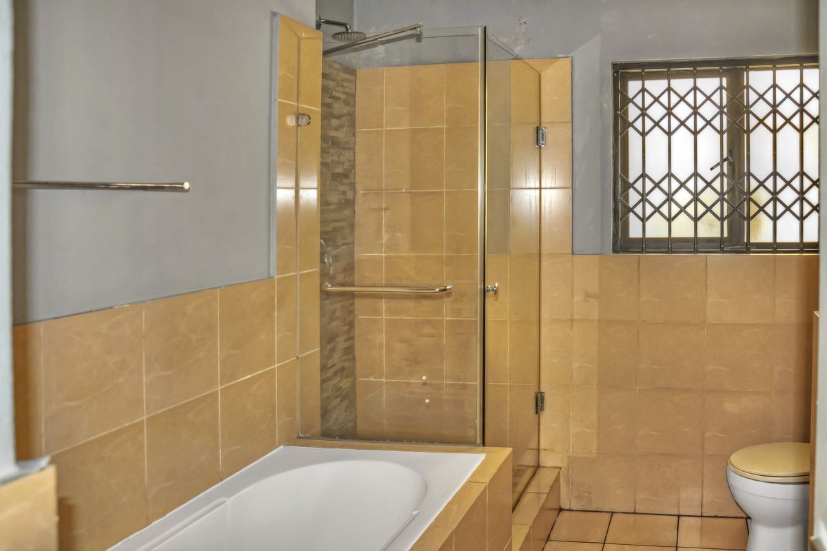 A functional bathroom featuring a built-in bathtub, a separate glass-enclosed shower, and neutral ceramic tiling throughout.