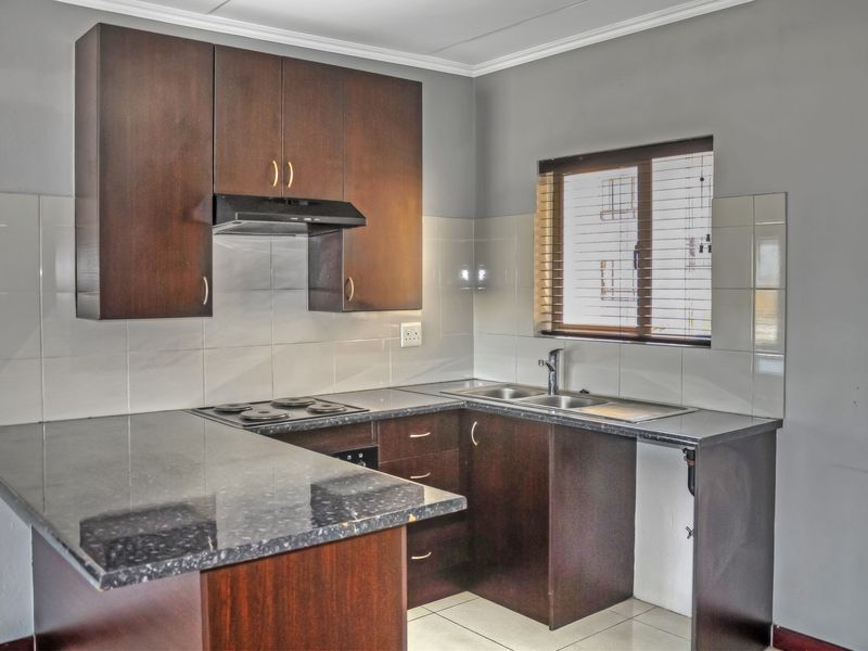 A functional kitchen featuring dark wood cabinetry, granite countertops, an electric hob with extractor fan, and a tiled splashback.
