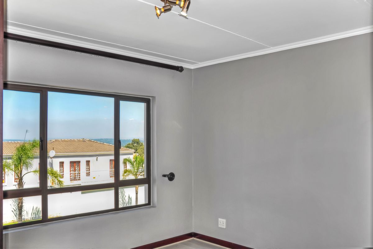 A bright, empty bedroom featuring neutral grey walls, modern aluminium window frames, and a ceiling-mounted spotlight fixture.