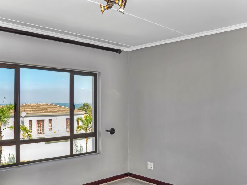 A bright, empty bedroom featuring neutral grey walls, modern aluminium window frames, and a ceiling-mounted spotlight fixture.