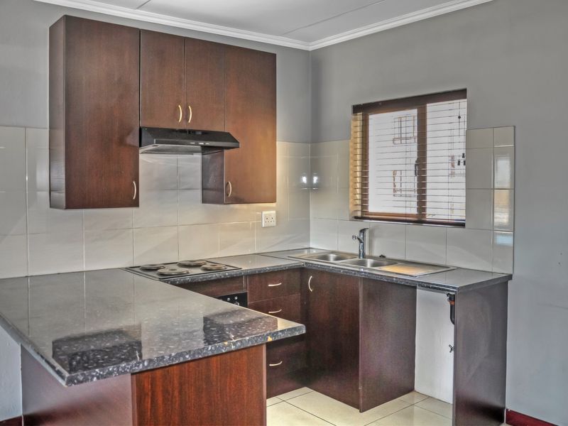 A functional kitchen featuring dark wood cabinetry, granite countertops, an electric hob with extractor fan, and a stainless steel sink with tiled backsplash.
