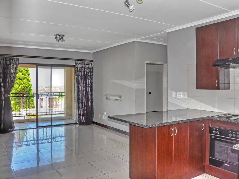 Open plan living area featuring a modern kitchen with dark wood cabinetry, granite countertops, built-in appliances, and direct access to a private balcony.